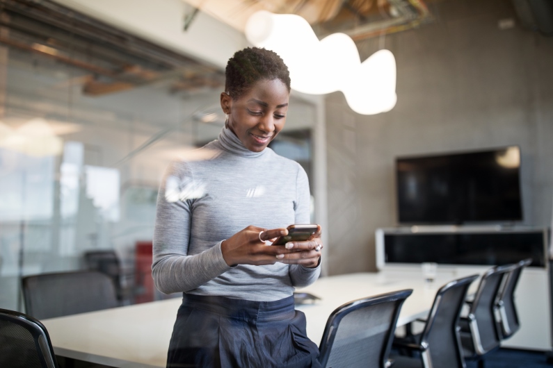 a person stands in a boardroom smiling at their phone