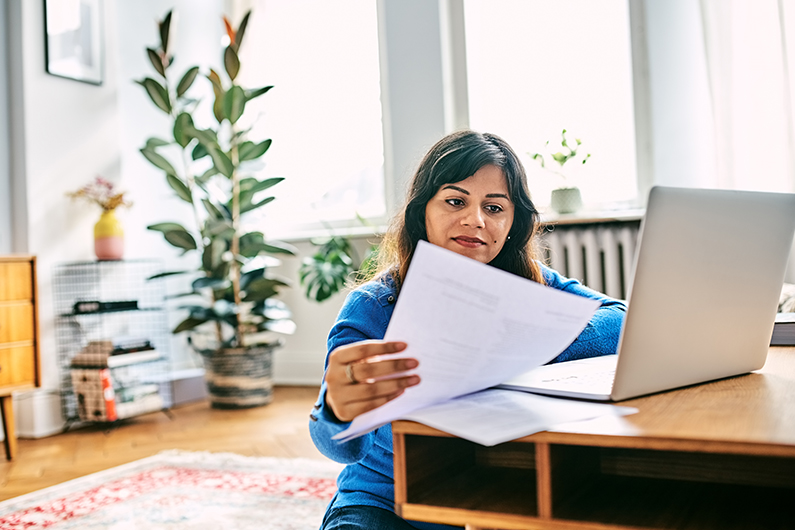 Woman with shoulder length hair sits at a wooden desk and calculates year-end finances at home.