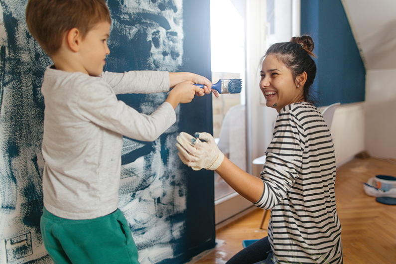 A mother and son paint a wall with blue paint in their home.
