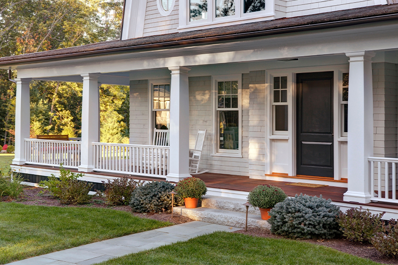 Front porch with white columns, black door, and landscaped garden.