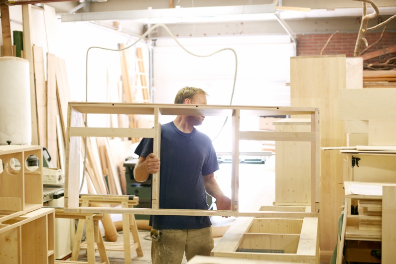 A man works in his woodworking workshop as a sole proprietor.