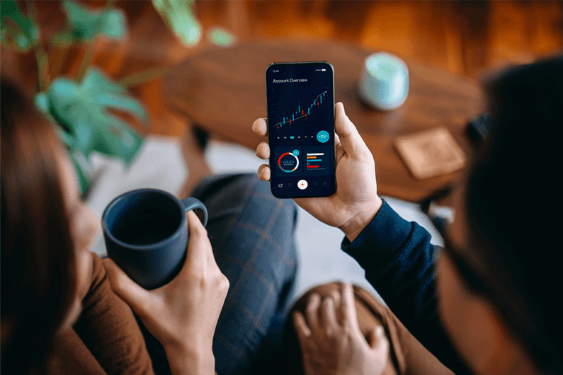 Two women sit on a couch and review an interest rate graph on their mobile phone.