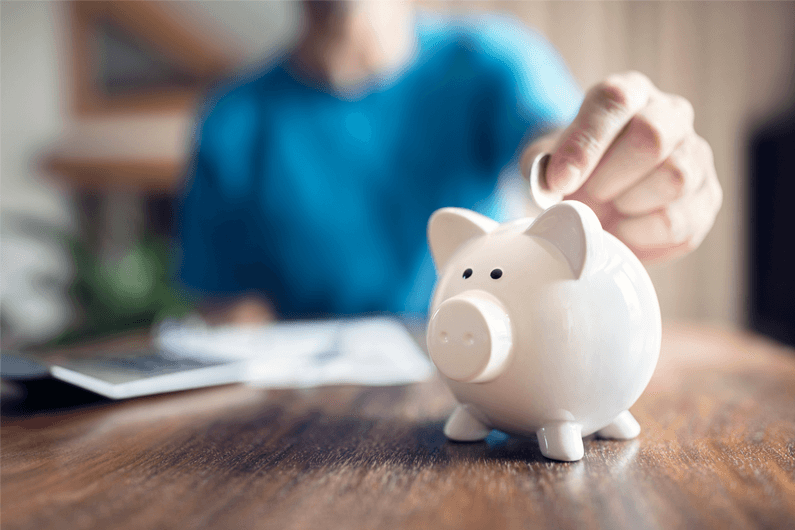 A woman wearing a blue sweater adds coins into a white piggy bank